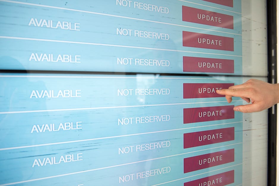 A person pointing at a digital screen displaying a schedule for garden maintenance bookings, with the screen showing multiple rows labeled 'AVAILABLE' and 'NOT RESERVED' alongside red 'UPDATE' buttons